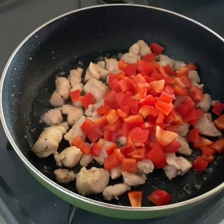 フライパンで炒めた鶏もも肉に赤パプリカを加えた様子