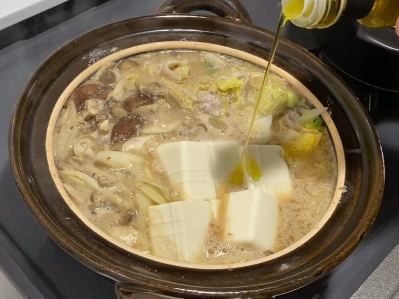 豚肉と白菜の豆乳ごまみそ鍋に白トリュフオイルを回し入れている様子