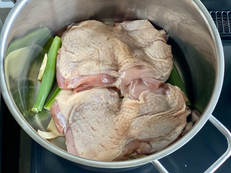 ステンレス鍋に入れた長ねぎの青い分部とスライスしょうがと下味をつけた鶏もも肉